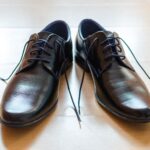 A pair of shiny, elegant black leather dress shoes with laces on a wooden floor.