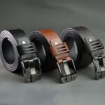 Three stylish leather belts with modern buckles on a gray background.