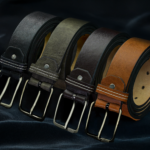 Set of luxurious leather belts in black, grey, brown, and tan on elegant fabric background.