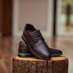 Stylish perforated leather shoes displayed elegantly on a rustic wooden stump indoors.